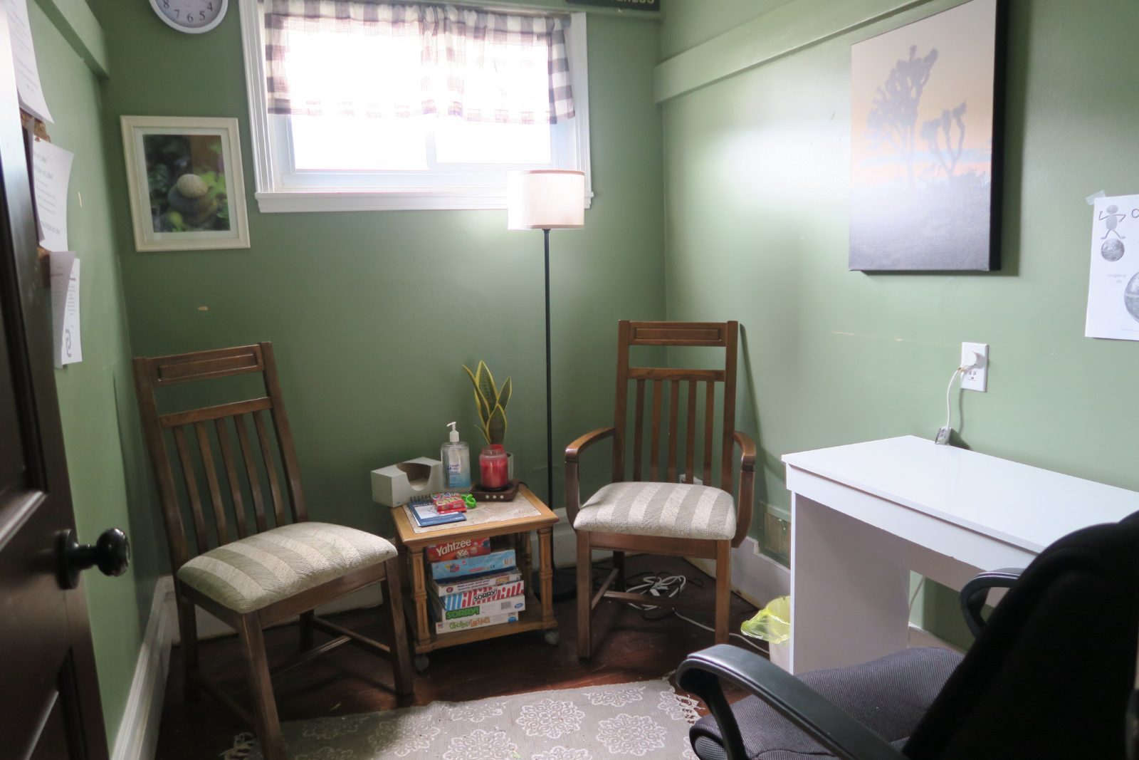 A green session room with two wooden chairs, a side table of books and a desk