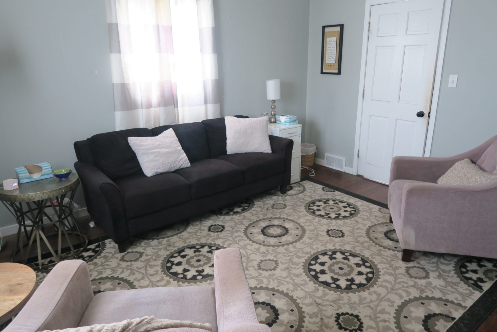 A soft grey therapy room with a dark sofa and two pink armchairs